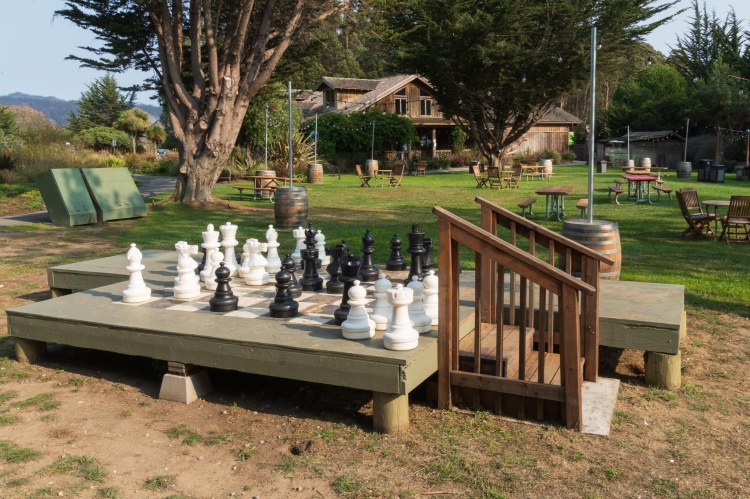Giant chess game on platform with grass and a building in the background